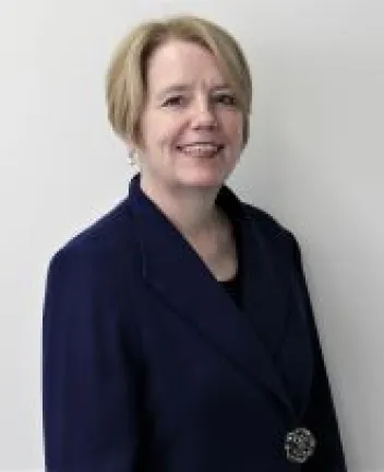 Professional woman in navy blazer smiling, neutral background