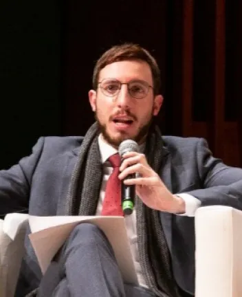 Man speaking into microphone while seated on stage