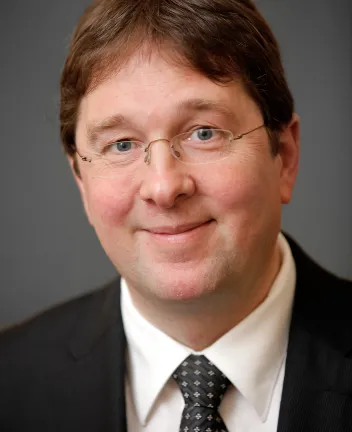 Professional headshot of man in suit and tie smiling